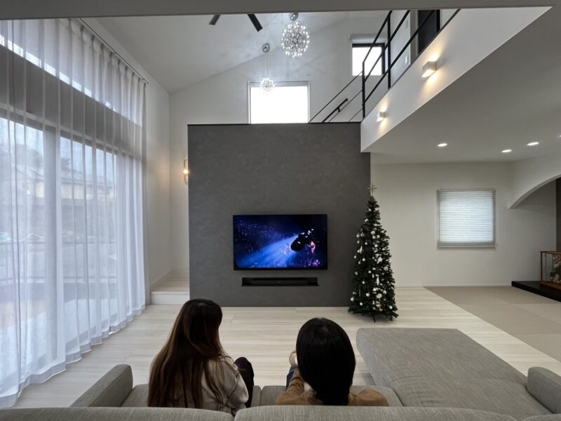 カーテンを開けて生活できる開放的な家の施工例紹介ページ。TVをご覧になるご夫婦の画像